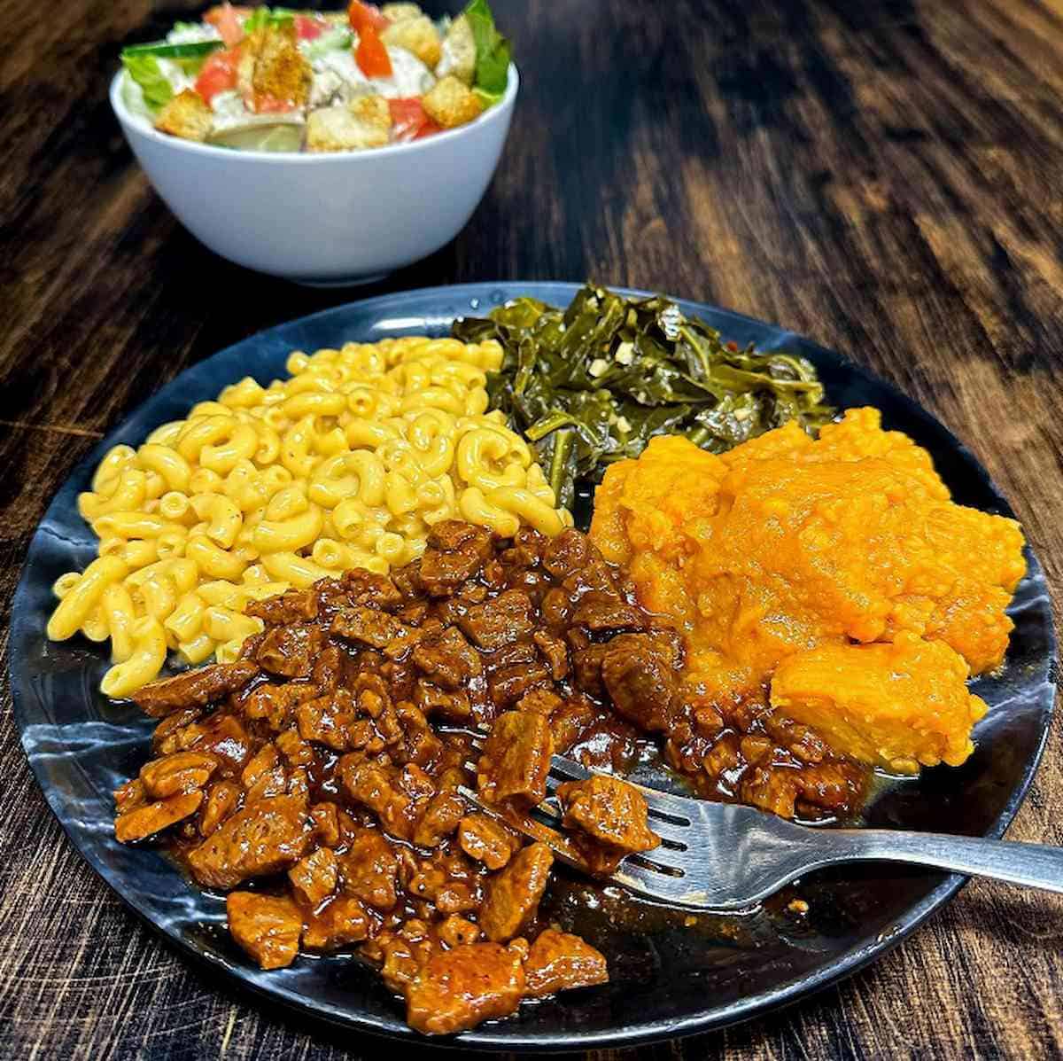 A vegan Southern plate including BBQ TVP, Mac & Cheese, collard greens and candied yams.