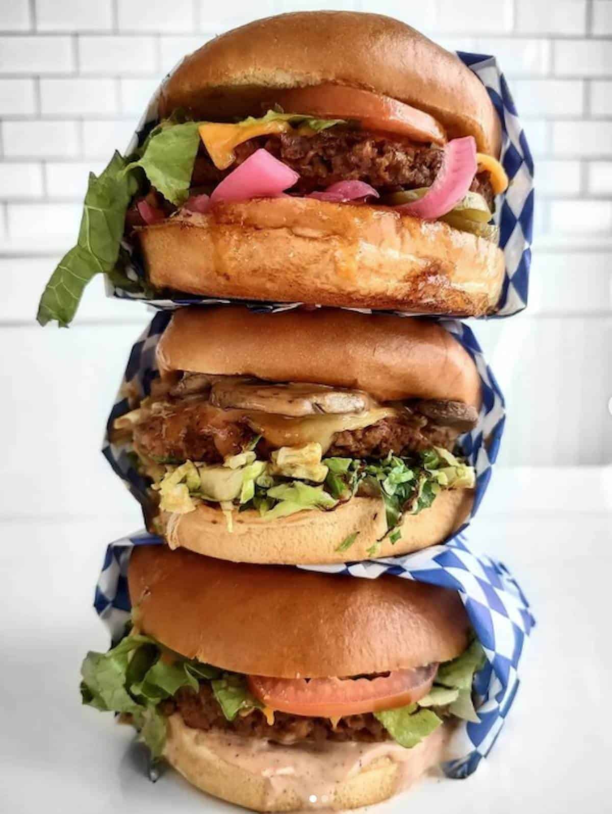 Three vegan burgers with various toppings stacked on one another.