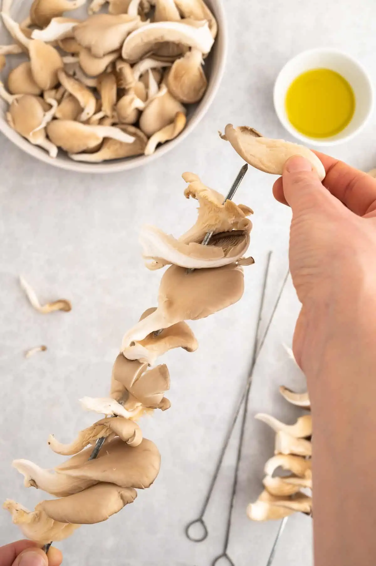 Oyster mushrooms being threaded onto a metal skewer.