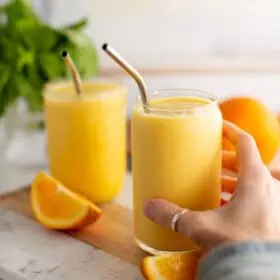 A hand reaching for an orange juice smoothie.