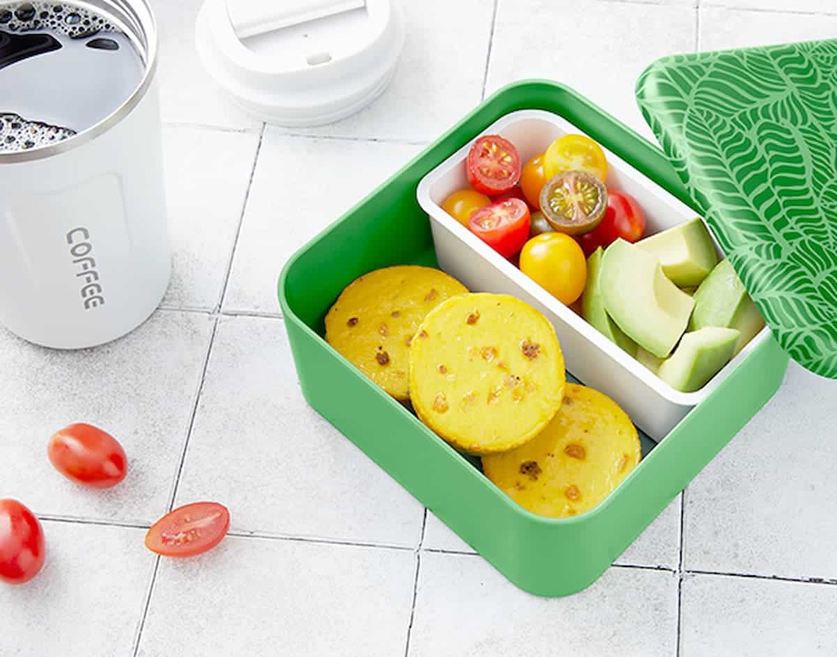 Simply Eggless Egg Bites in a lunch box with cherry tomatoes and avocado.