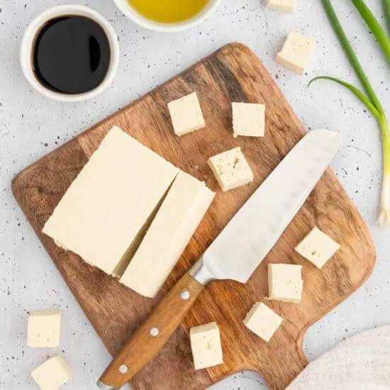 Tofu cut and cubed on a wooden cutting board.