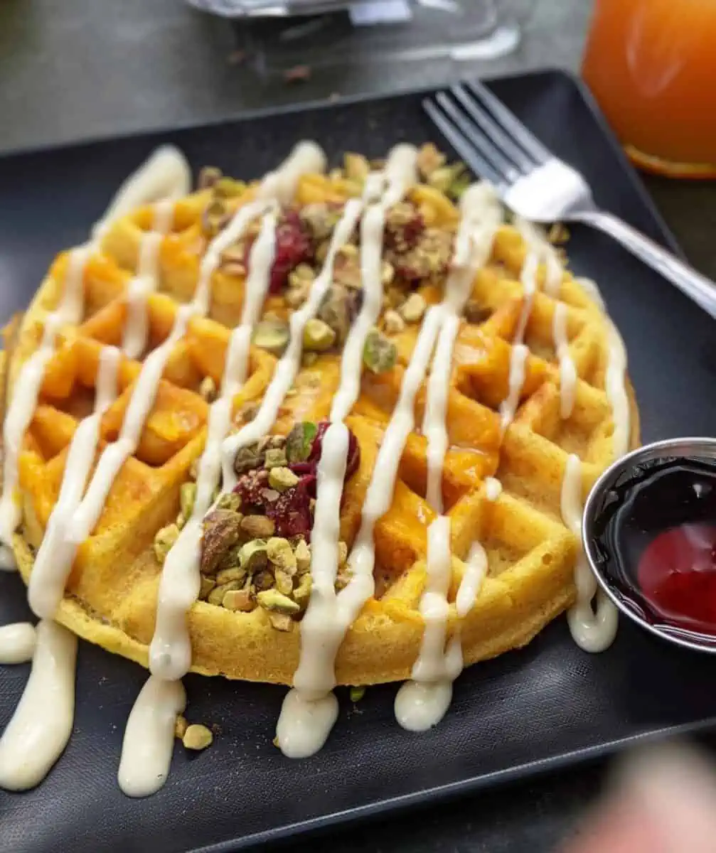 Vegan waffle topped with pistachios, cranberries and icing.