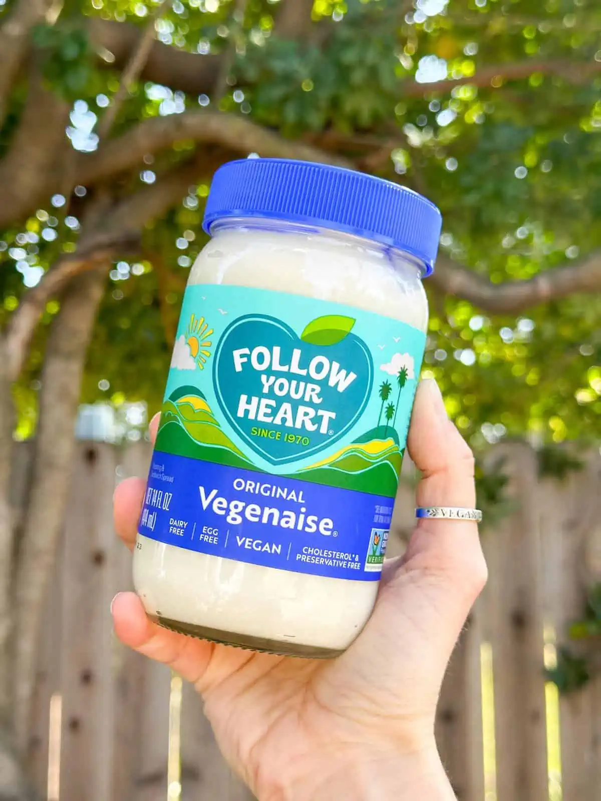 Woman holding out a new jar of the original Follow Your Heart Veganaise with the blue lid and label. 