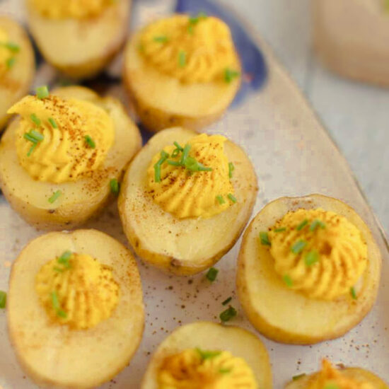 A plate of vegan deviled eggs made with roasted potatoes, piped with a turmeric-spiced filling, and sprinkled with paprika and chives.