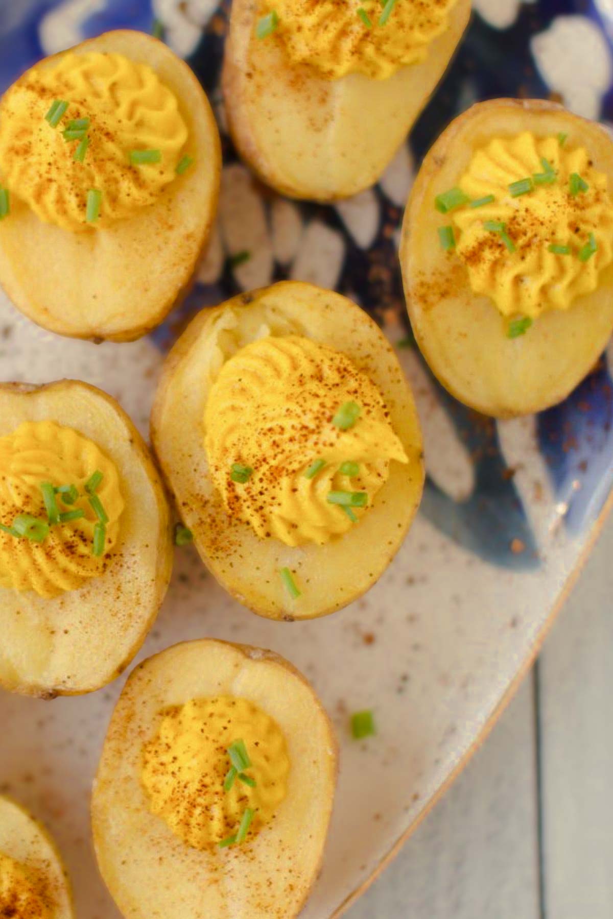 A close-up of vegan deviled eggs made with baby potatoes, topped with a creamy filling, paprika, and fresh chives on a speckled plate.