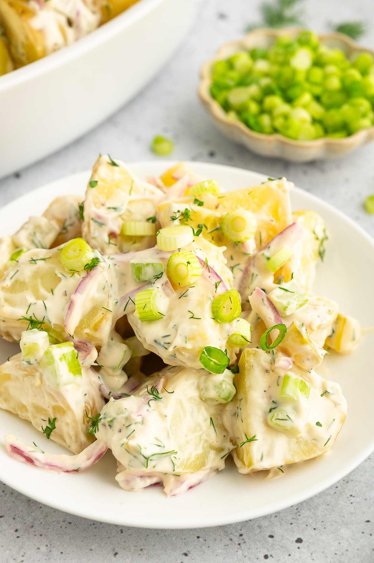 Vegan potato salad on a plate, topped with sliced green onion.