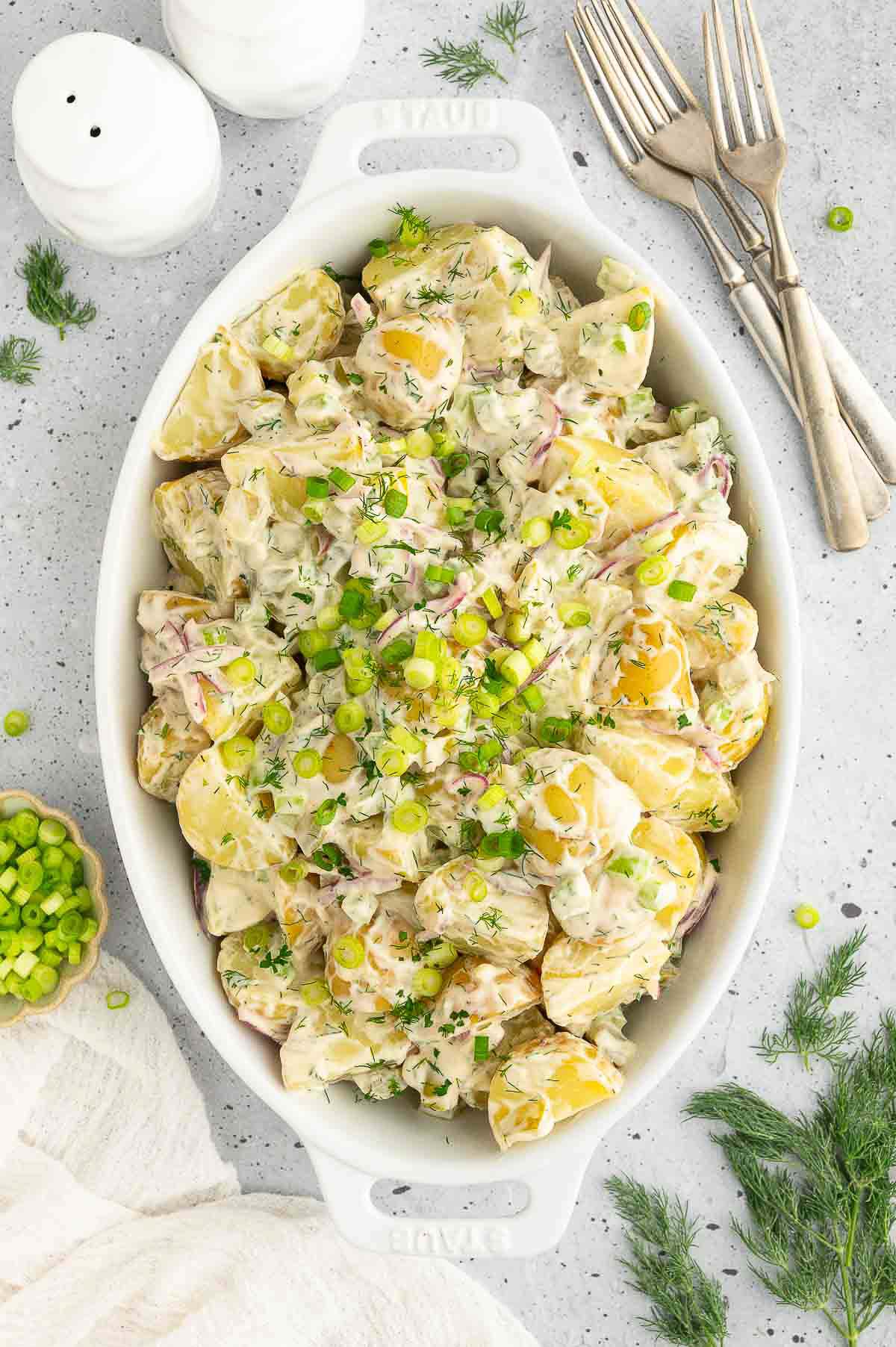 Vegan potato salad in a casserole dish, topped with sliced green onion and fresh dill.