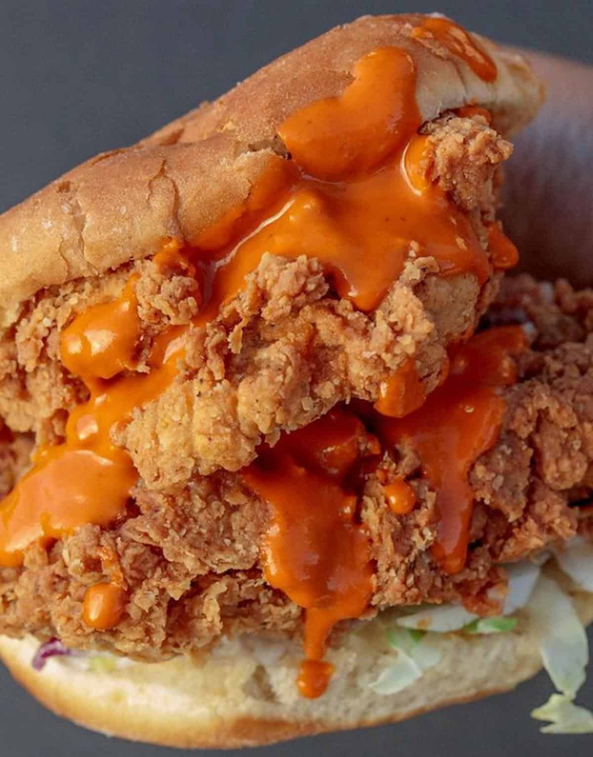 Vegan chicken sandwich with spicy sauce dripping down the sides.