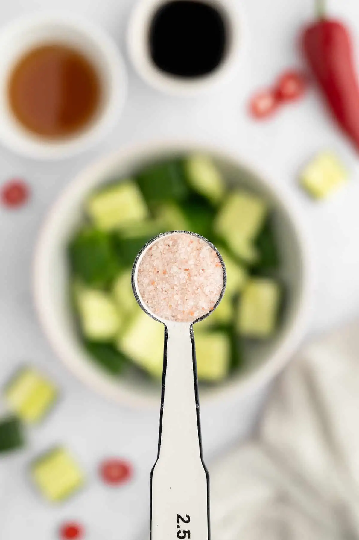 A spoonful of salt held over a bowl of chopped cucumber.