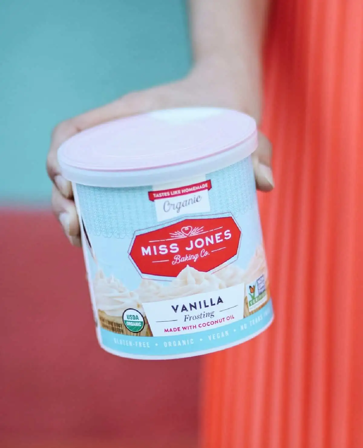 A woman in an orange pleated skirt holding a can of Miss Jones vanilla frosting. 
