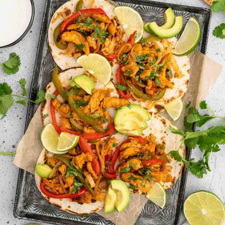 A tray of vegan fajitas with lime wedges and avocado slices.