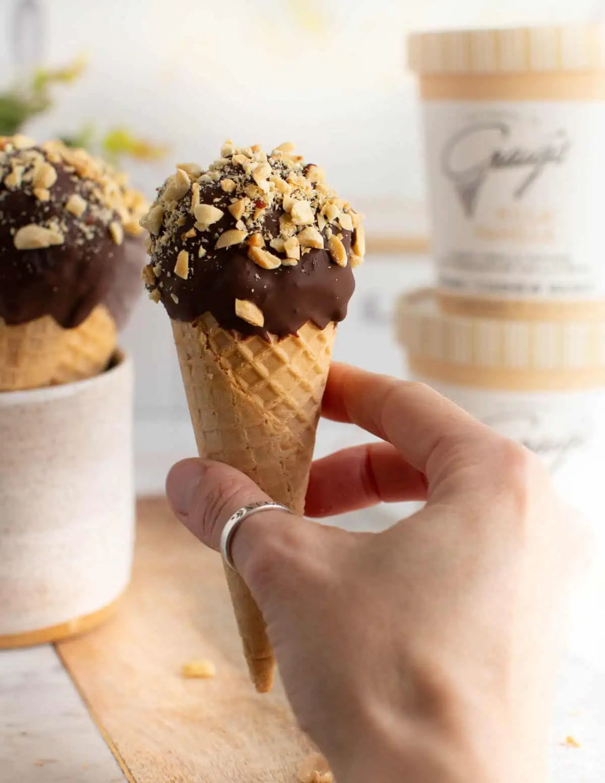 Vegan woman holding out a homemade drumstick in her hand with Craig's dairy-free cashew ice cream pints in the background. 
