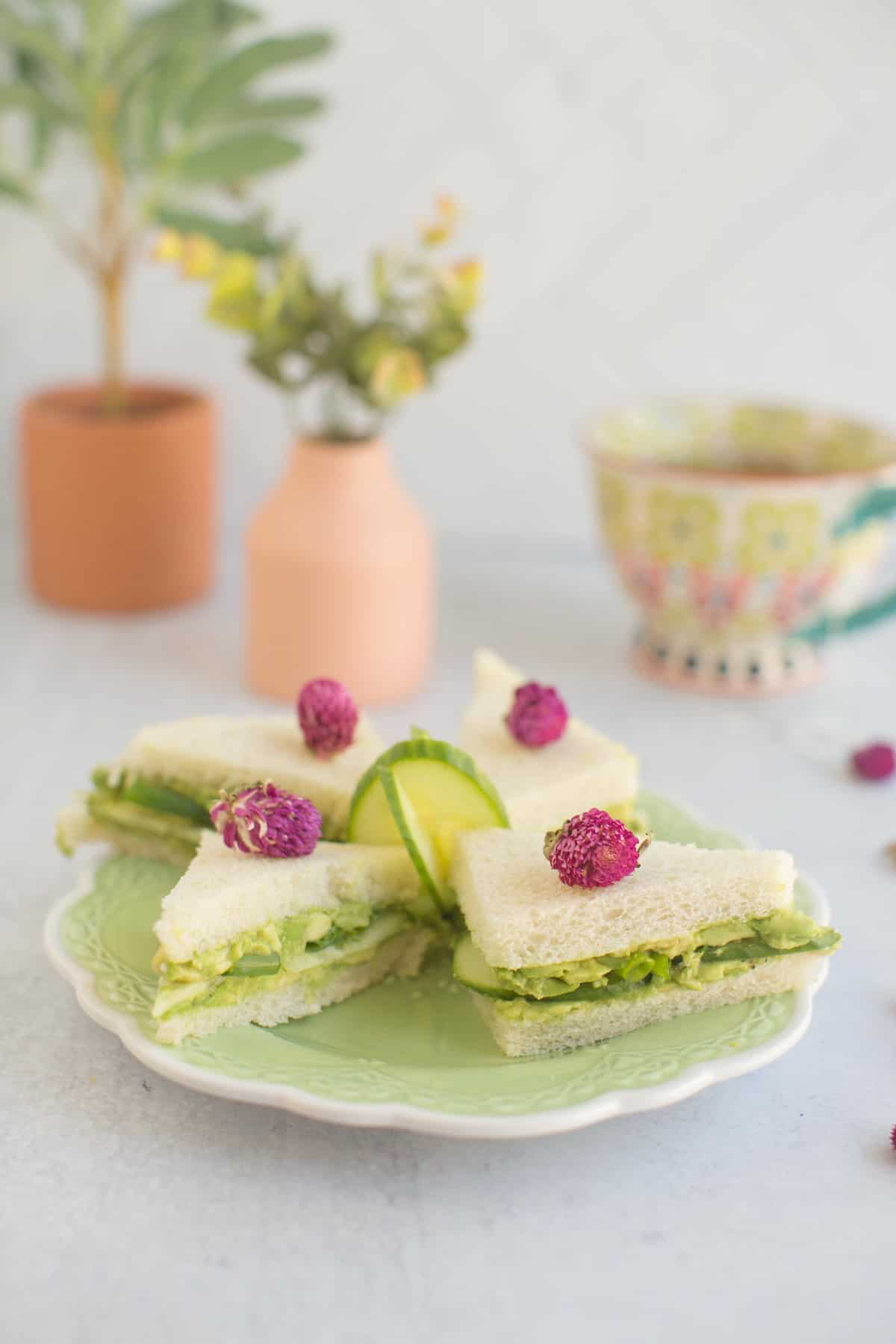 Four vegan tea sandwiches on a plate with a tea cup in the background.