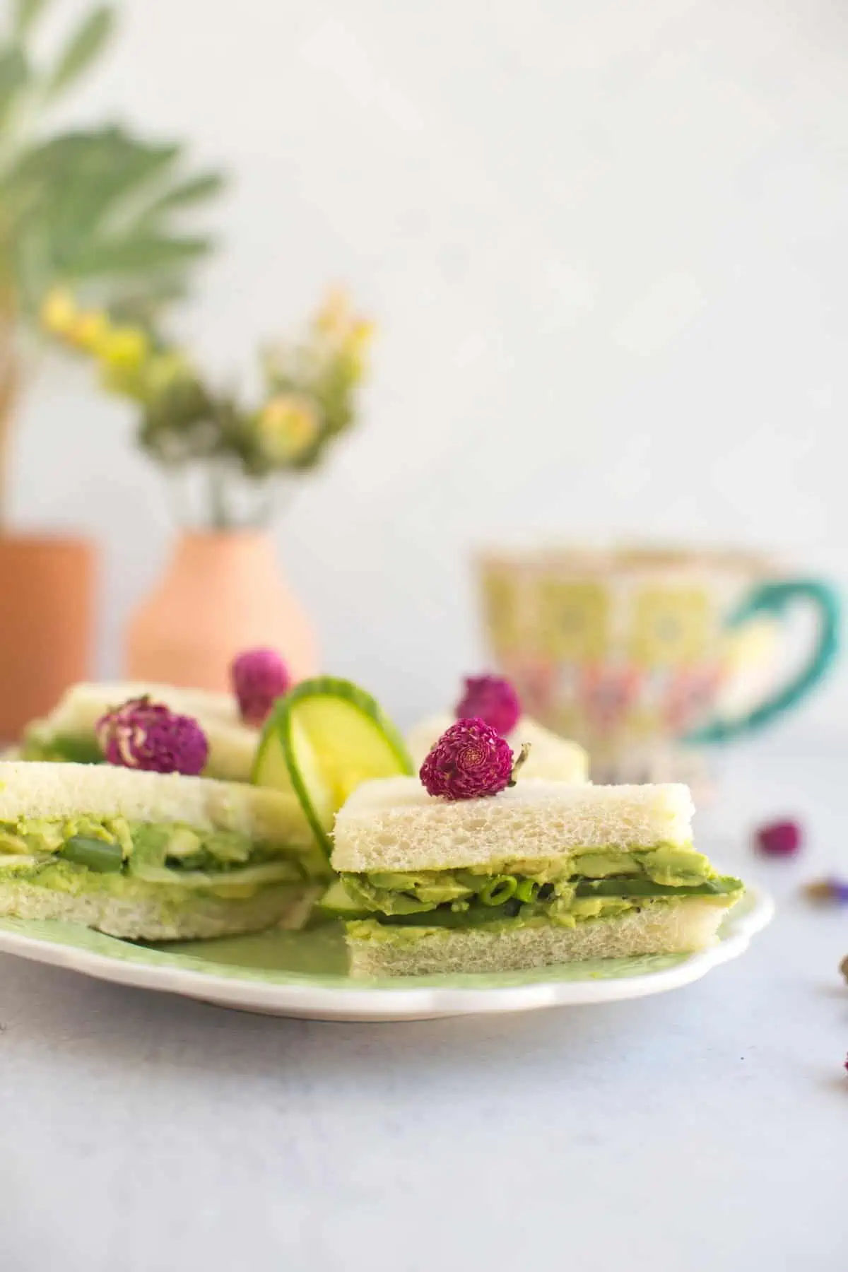 Side view of vegan afternoon tea sandwiches on a plate with a tea cup in the background.