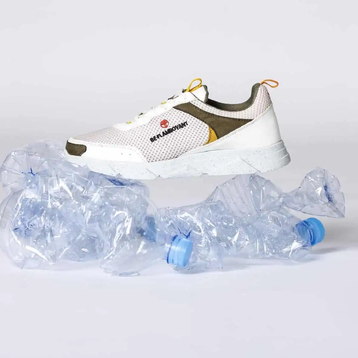 A single off white and brown vegan sneaker sitting on top of two crushed, empty plastic water bottles.