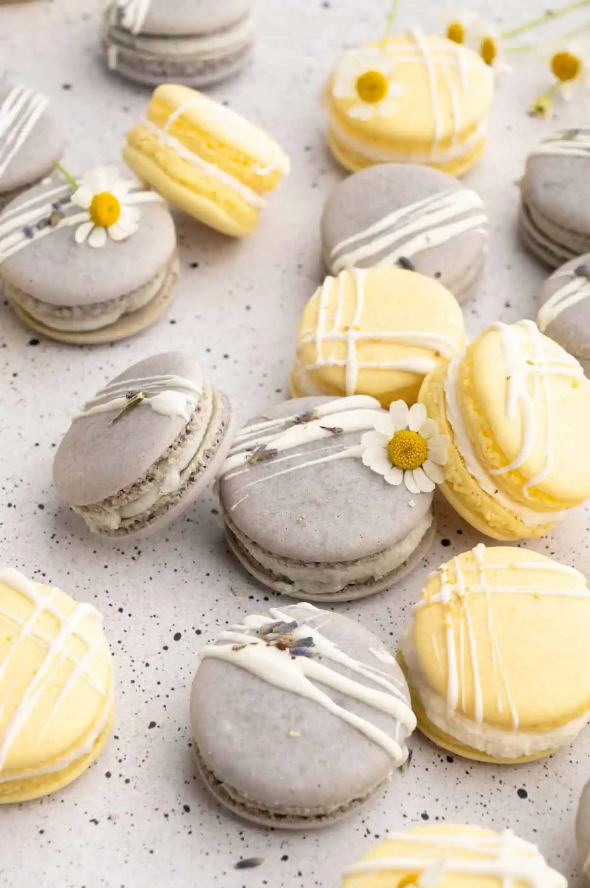 Yellow and purple vegan macarons in a cluster, topped with vegan white chocolate drizzle and edible flowers.