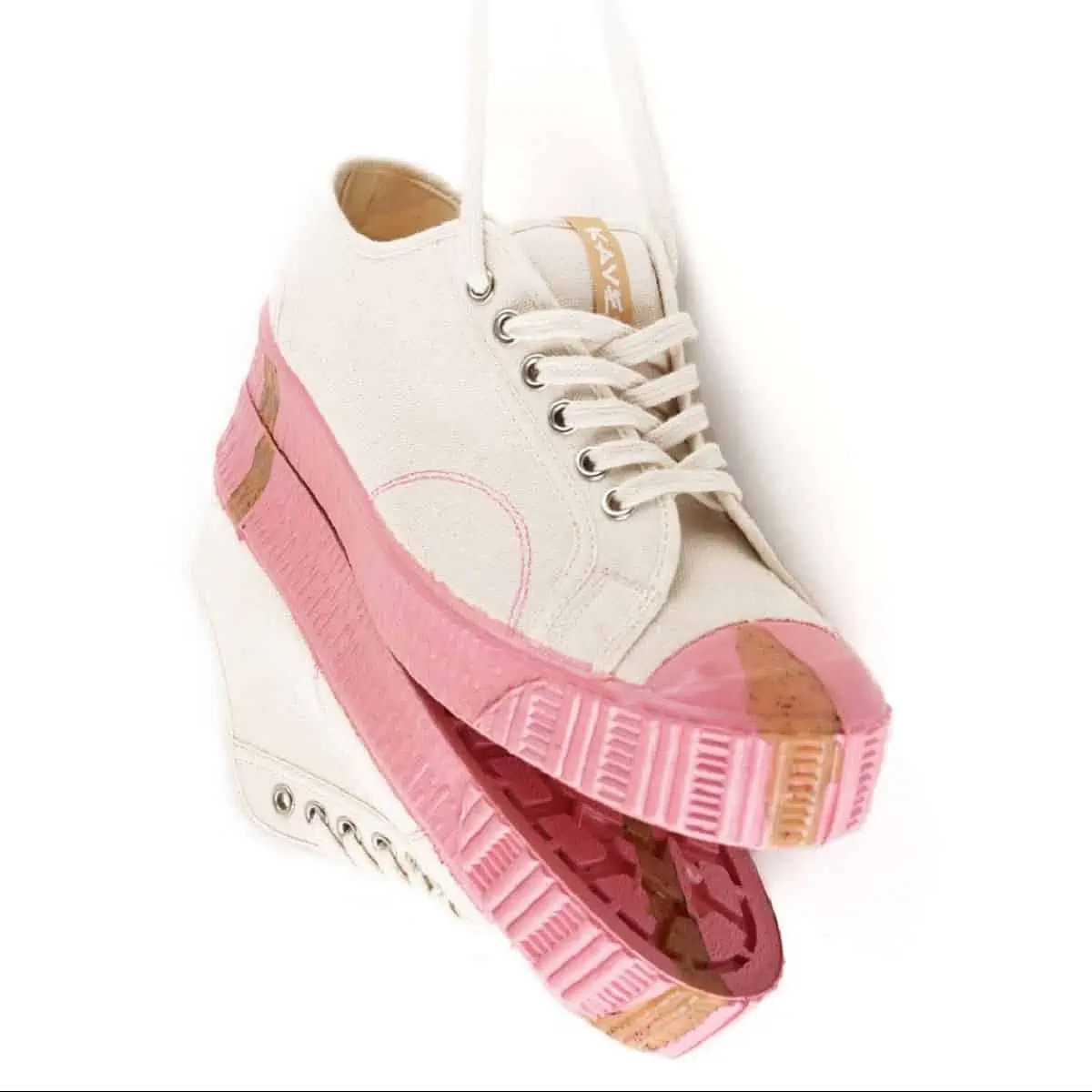 A pair of pink and cream Kave Footwear vegan sneakers hanging up by the laces against a white background.