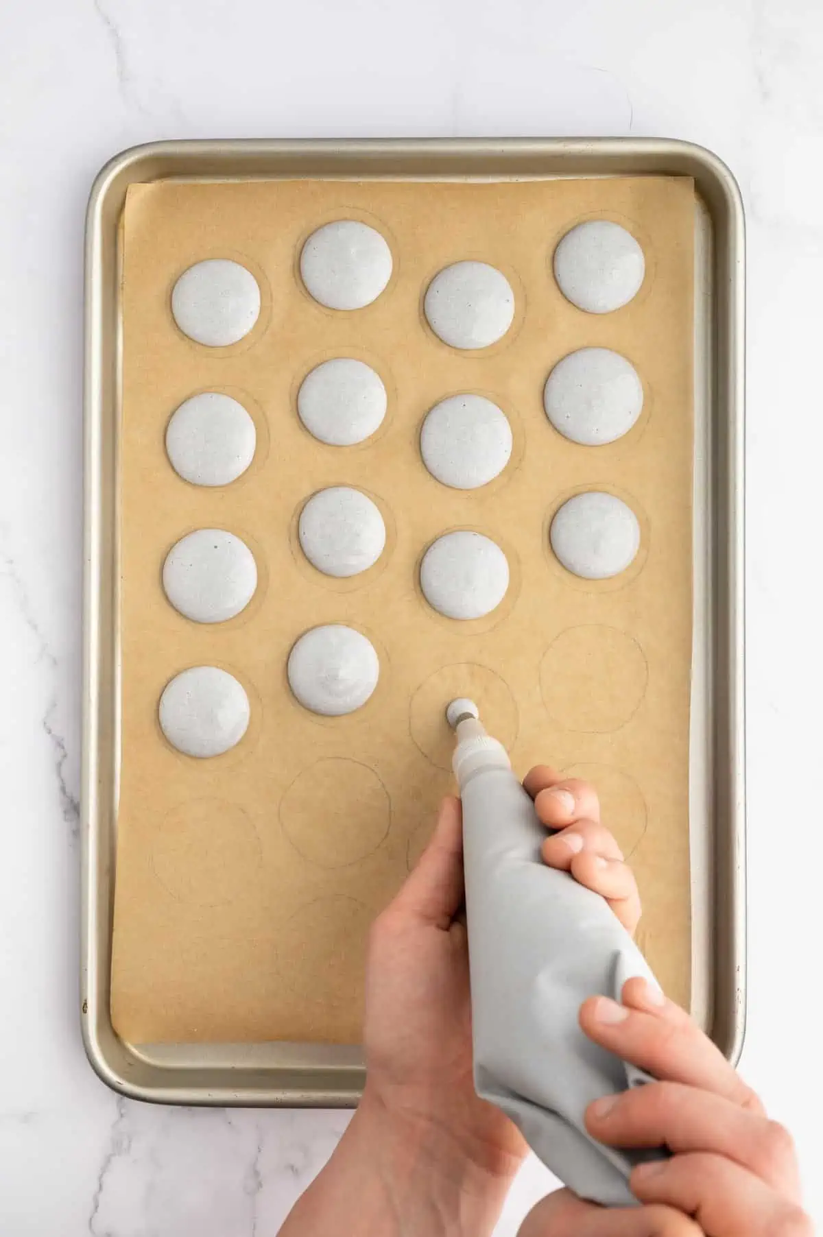 Piping vegan macaron batter onto a prepared baking sheet.