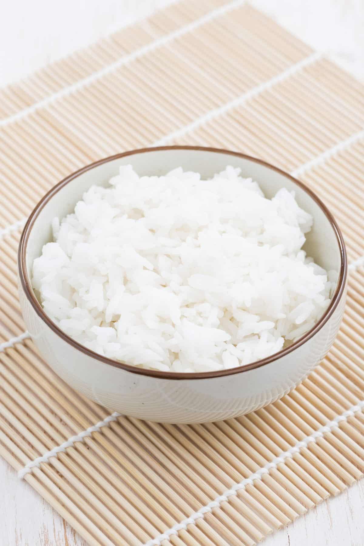 A bowl of sushi rice on a bamboo mat.