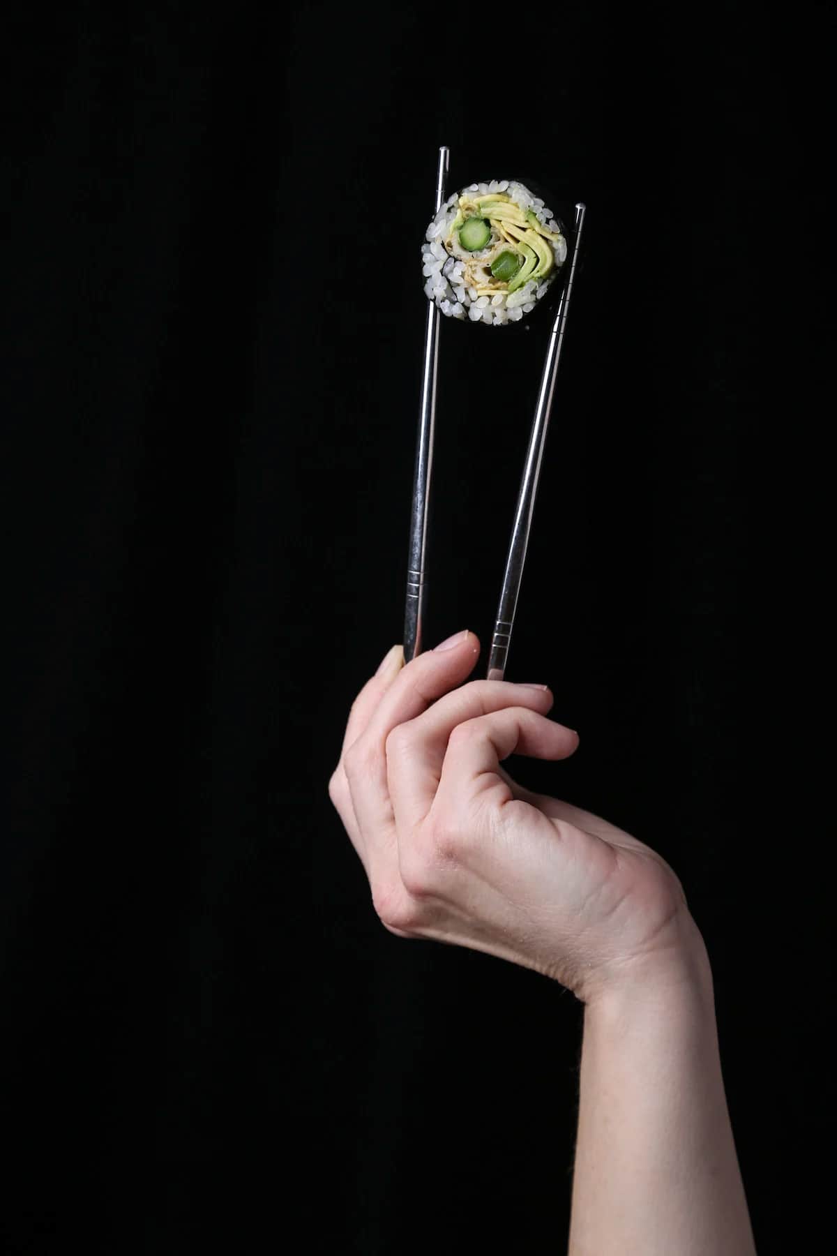 Chopsticks holding an avocado and asparagus sushi roll.