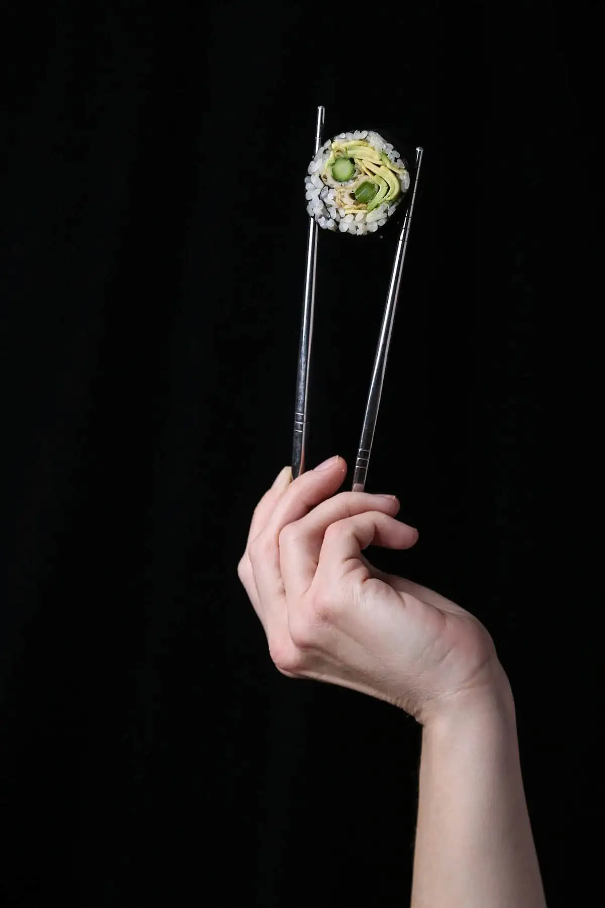 Chopsticks holding an avocado and asparagus sushi roll.