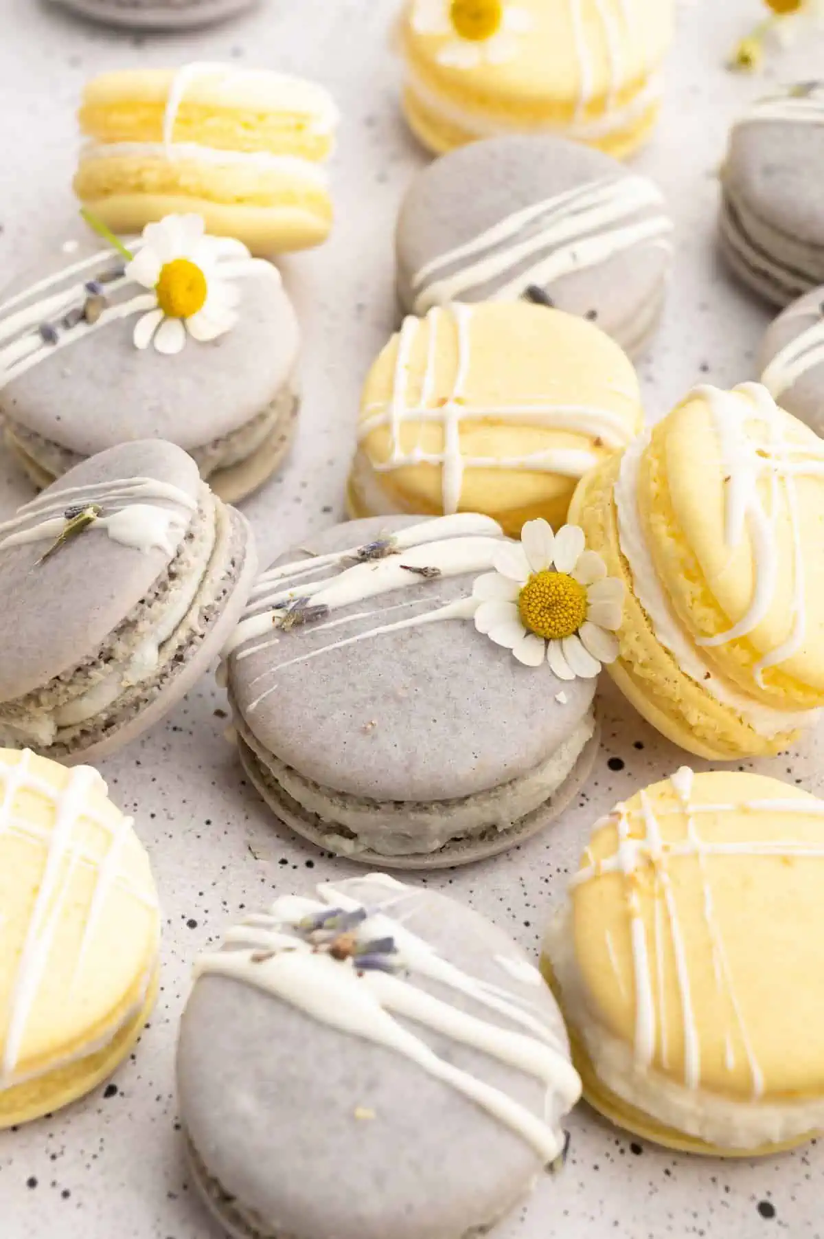 Yellow and purple vegan macarons in a cluster, topped with vegan white chocolate drizzle and edible flowers.