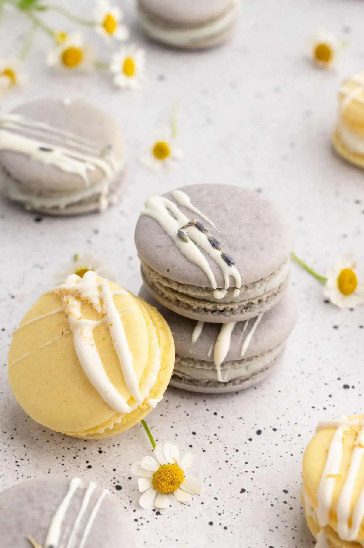 Two purple vegan macarons stacked with a yellow macaron resting against them, surrounded by edible flowers.