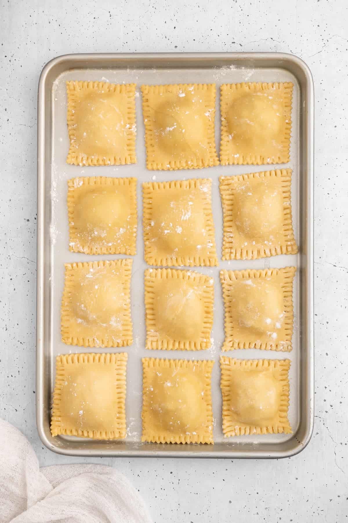 Prepped ravioli lined up on a baking sheet.