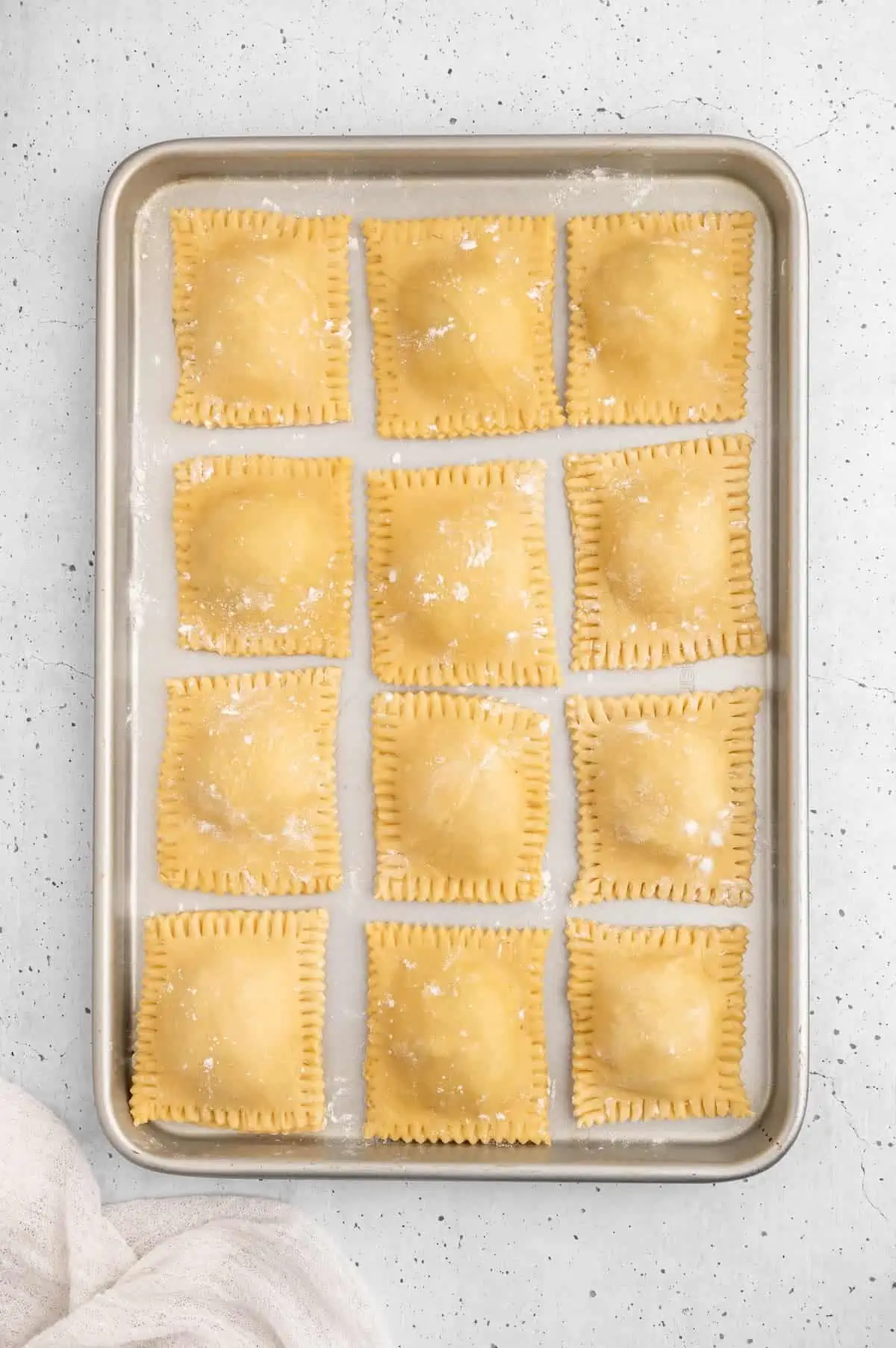 Prepped ravioli lined up on a baking sheet.