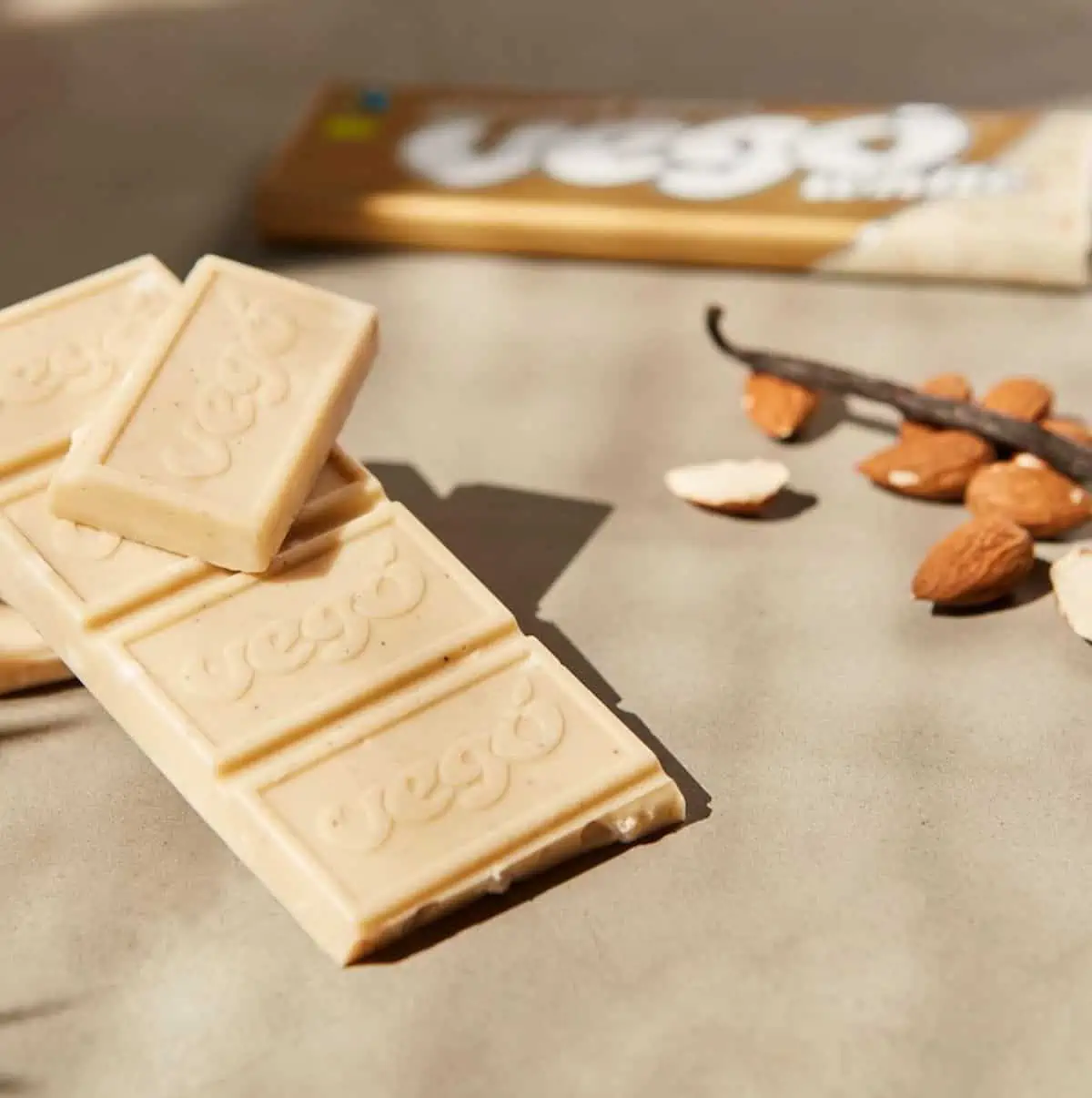 A bar of Vego white almond bliss chocolate next to raw almonds and vanilla beans.