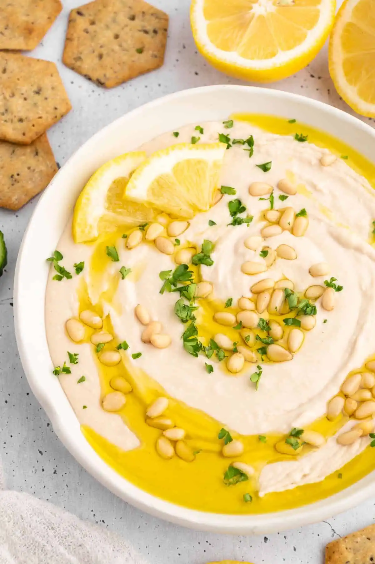 A bowl of white bean hummus dip, garnished with olive oil and pine nuts.