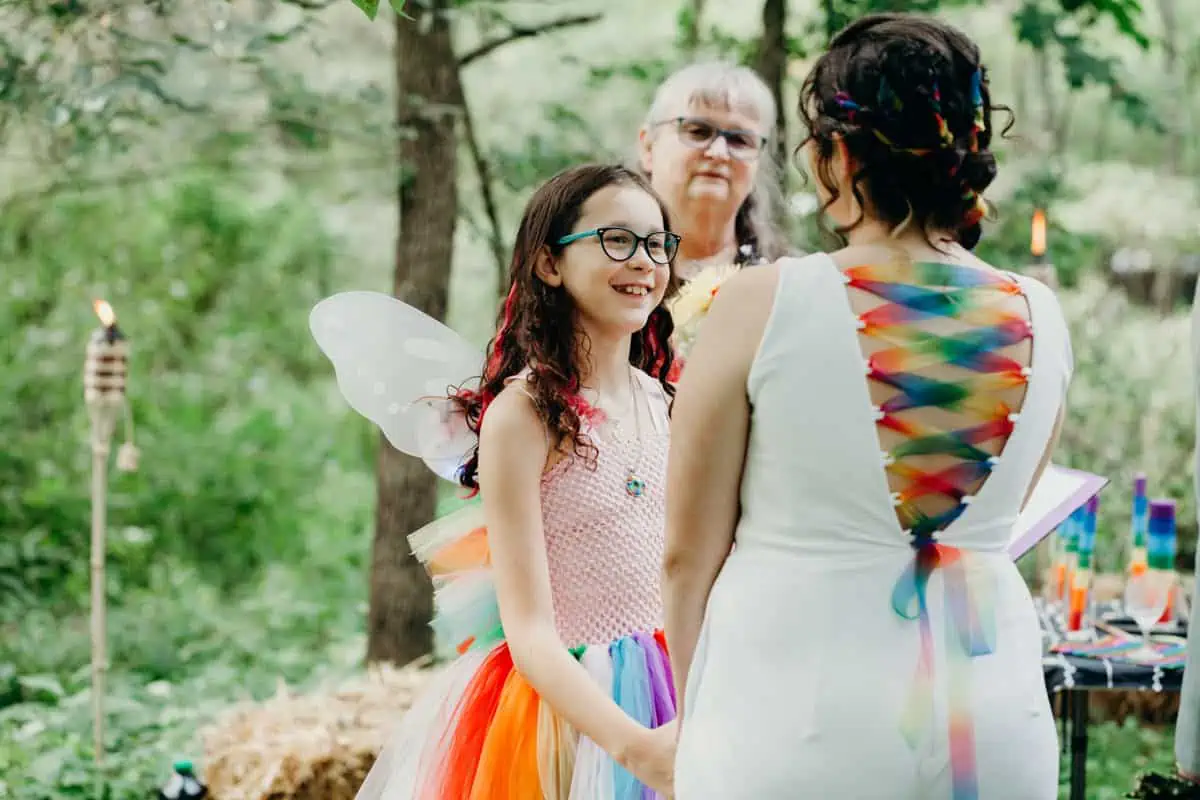 Beautiful rainbow wedding dress jumpsuit with colorful flower girl in woodland outdoor wedding.