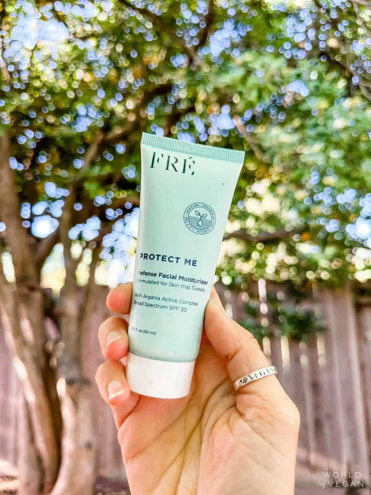Holding out the pale blue tube of vegan face sunscreen designed for active women from the brand Fre. 