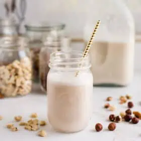 Plant-based milk in a mason jar surrounded by raw nuts.