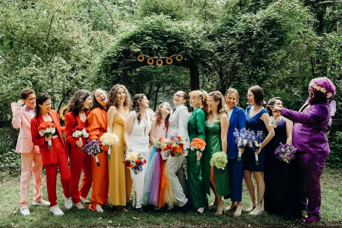 Photo of the best people dressed in colorful rainbow wedding party outfits in the woods.