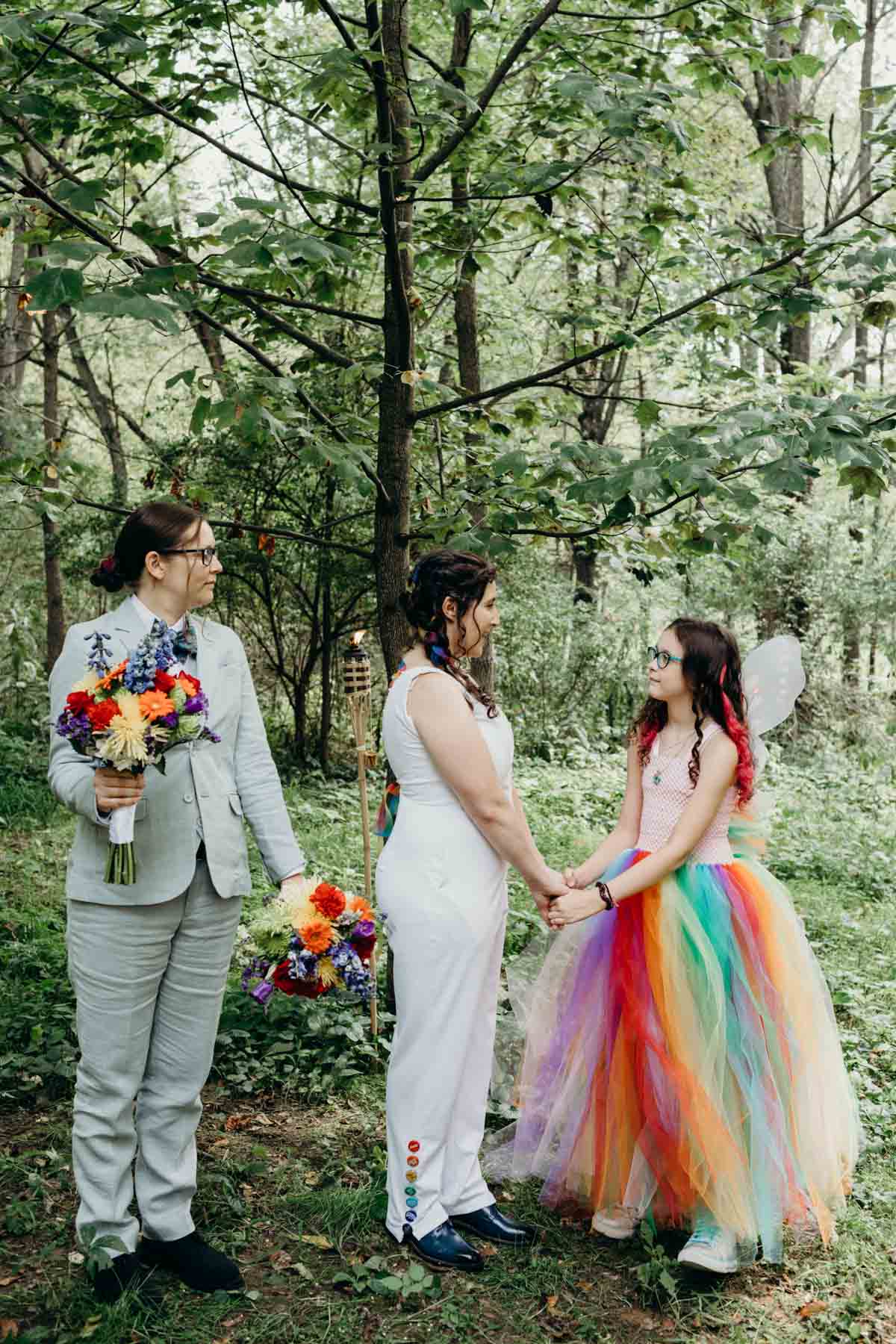 Bride saying vows to her stepdaughter in woodland forest wedding with rainbow wedding dress outfits. 