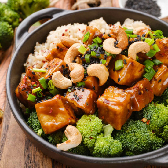Crispy szechuan tofu in a bowl with rice, broccoli, and topped with cashews.