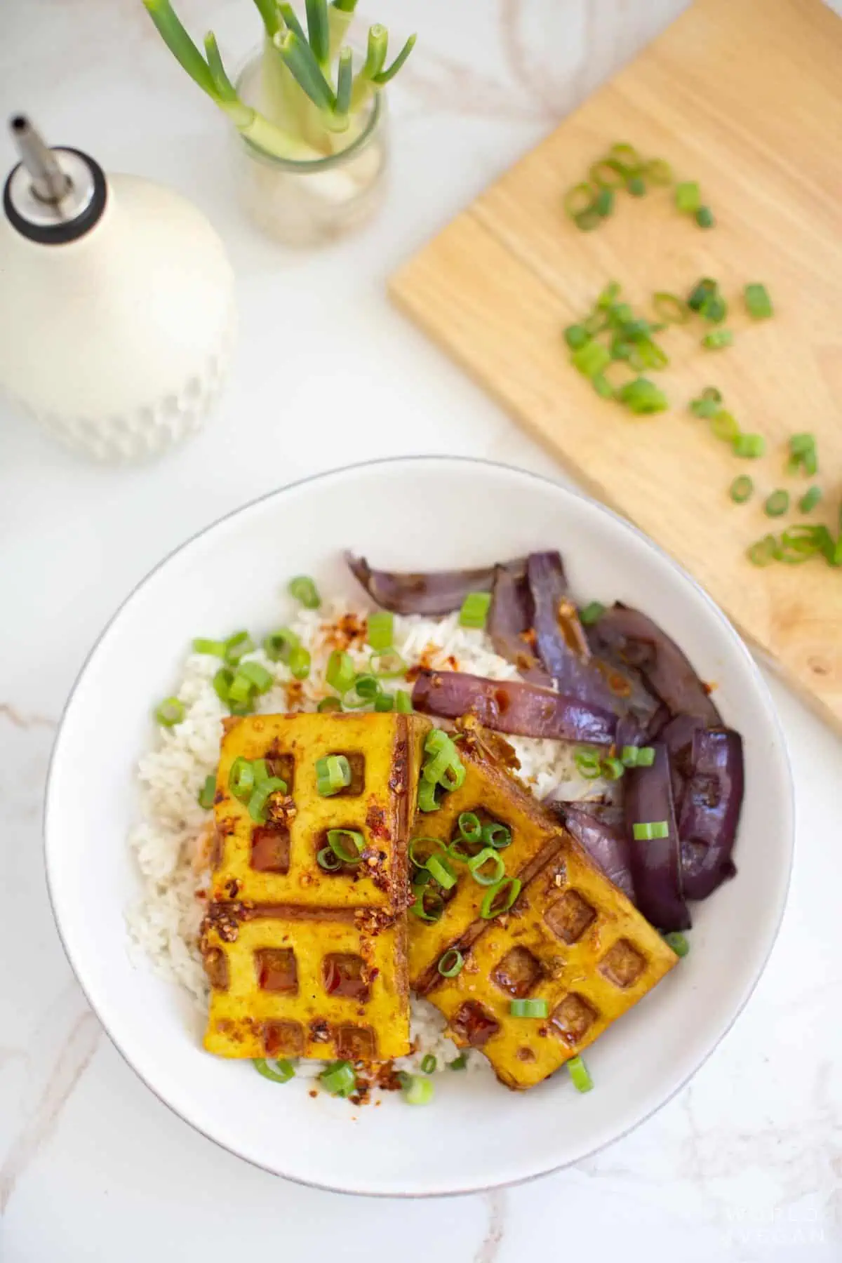 Scaled back flatlay photo of tofu waffles with green onions chopped on a cutting board. 