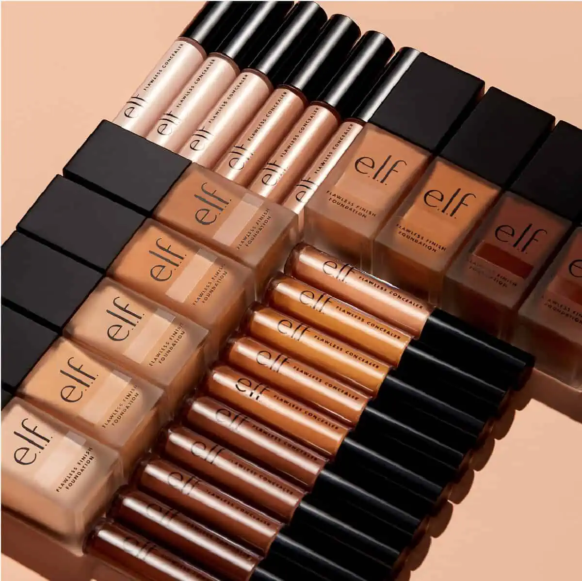 A collection of E.L.F. Cosmetics' vegan and cruelty-free Flawless Foundation and Concealer bottles laying on their sides in rows perpendicular to each other on a peach colored background.