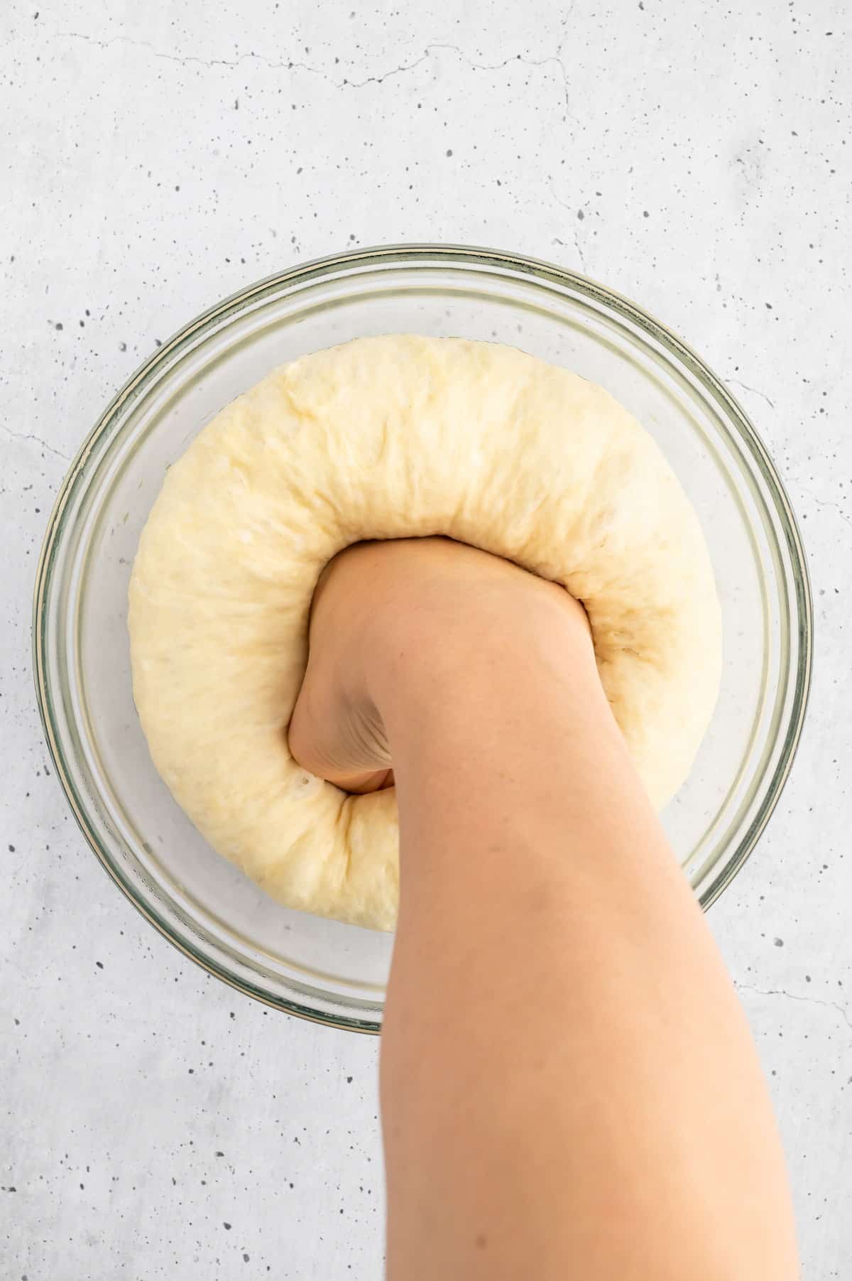 Pesto bread dough being punched down into a bowl.