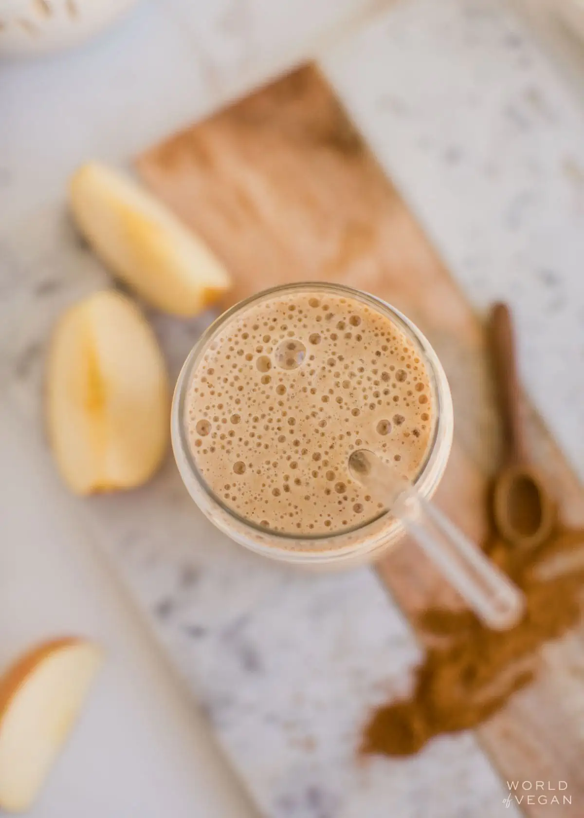 Overhead view of the apple banana smoothie in a glass with a straw, surrounded by various ingredients.