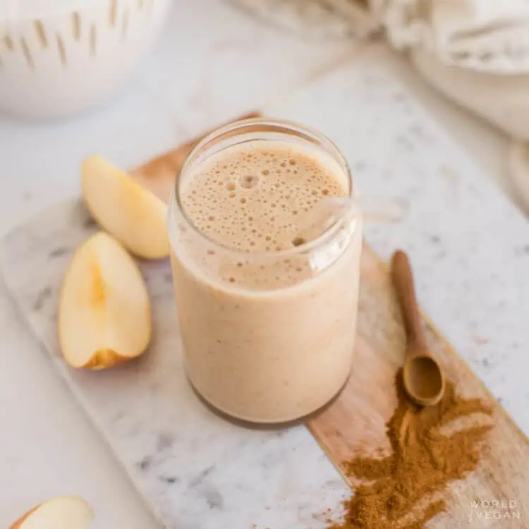 Apple banana smoothie in a glass next to sliced apples and cinnamon.
