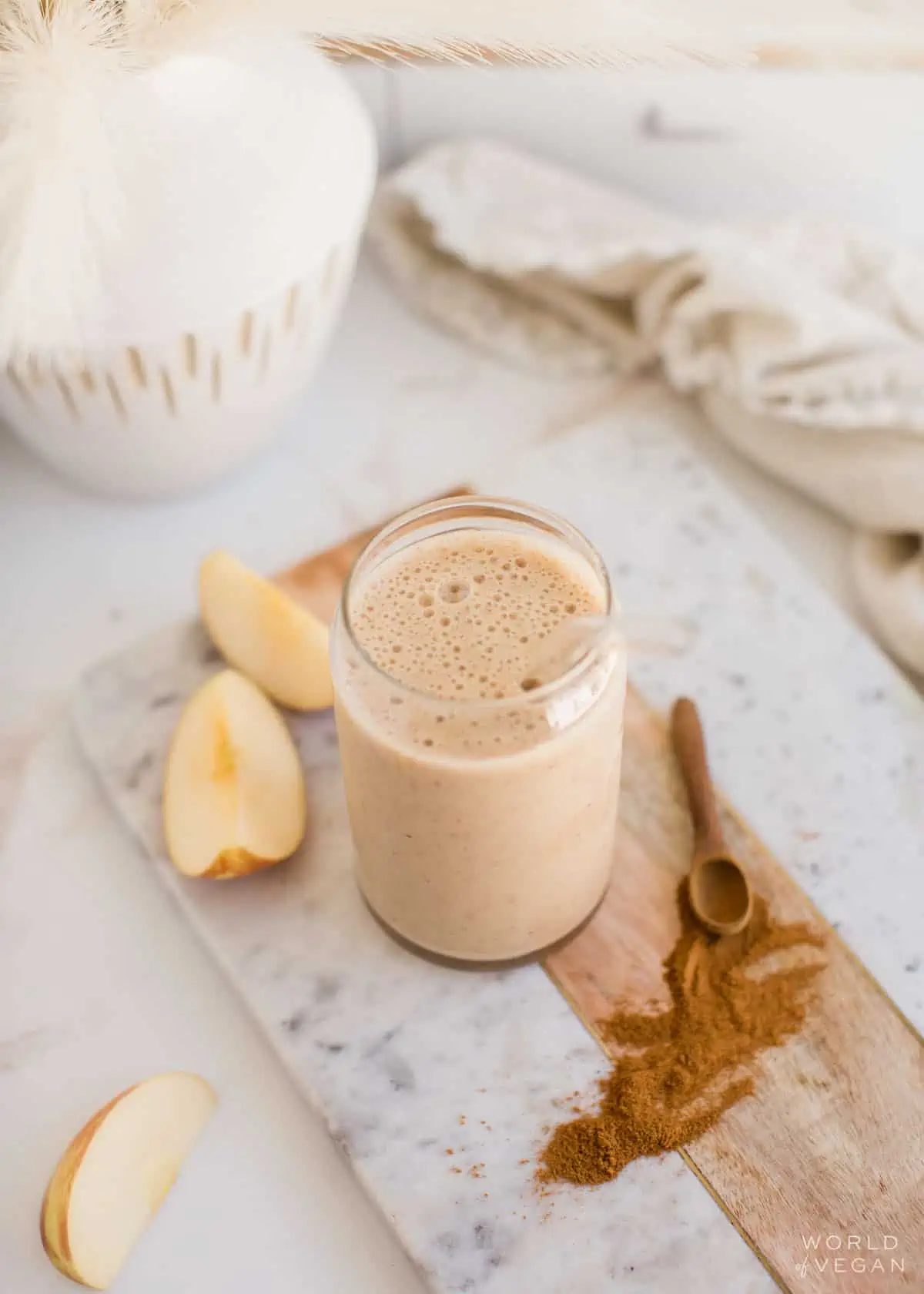 Apple banana smoothie in a glass next to sliced apples and cinnamon.