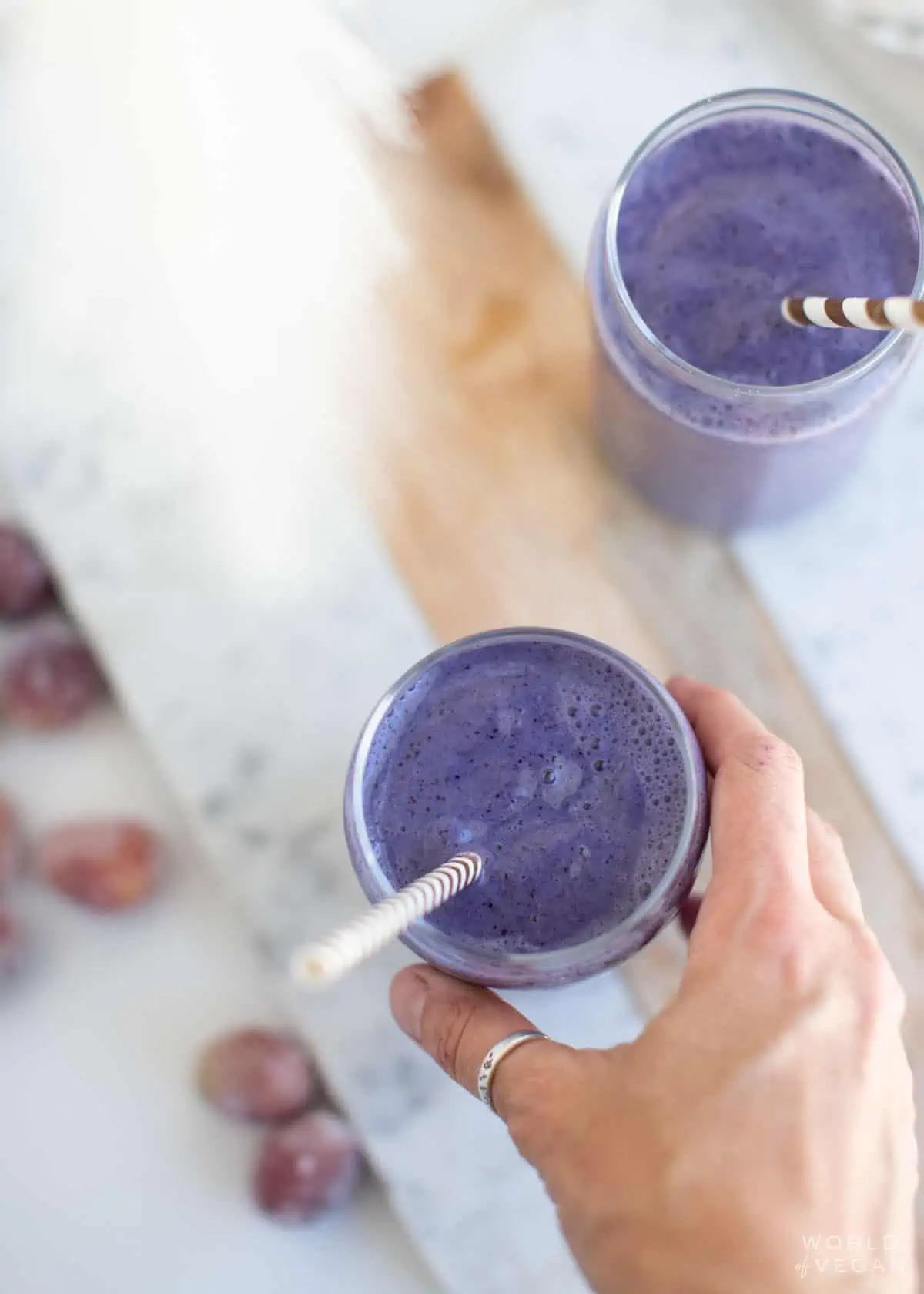A hand reaching for a glass filled with the purple grape smoothie.