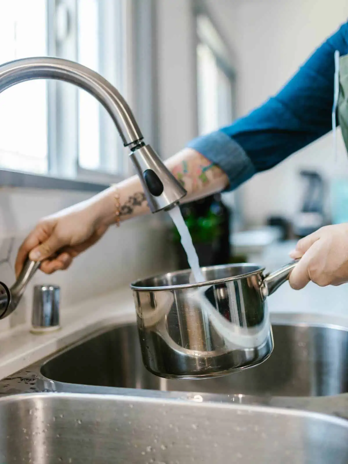 Woman pouring tap water from the sink into a pot of water for boiling. 