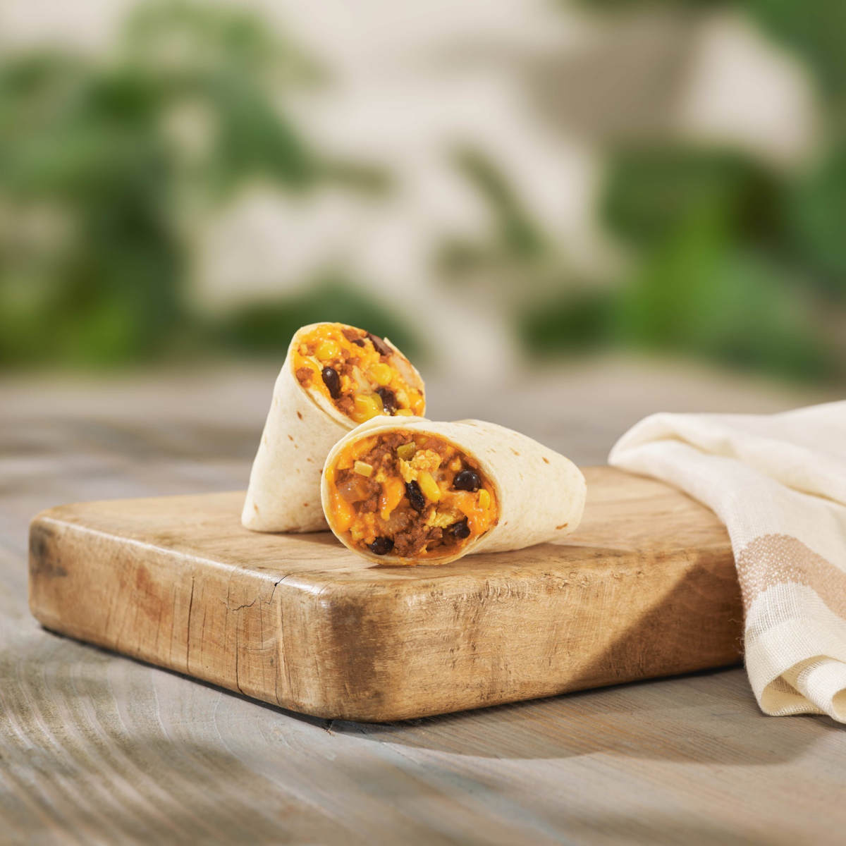 Peet's vegan breakfast burrito sliced in half on a wooden cutting board.