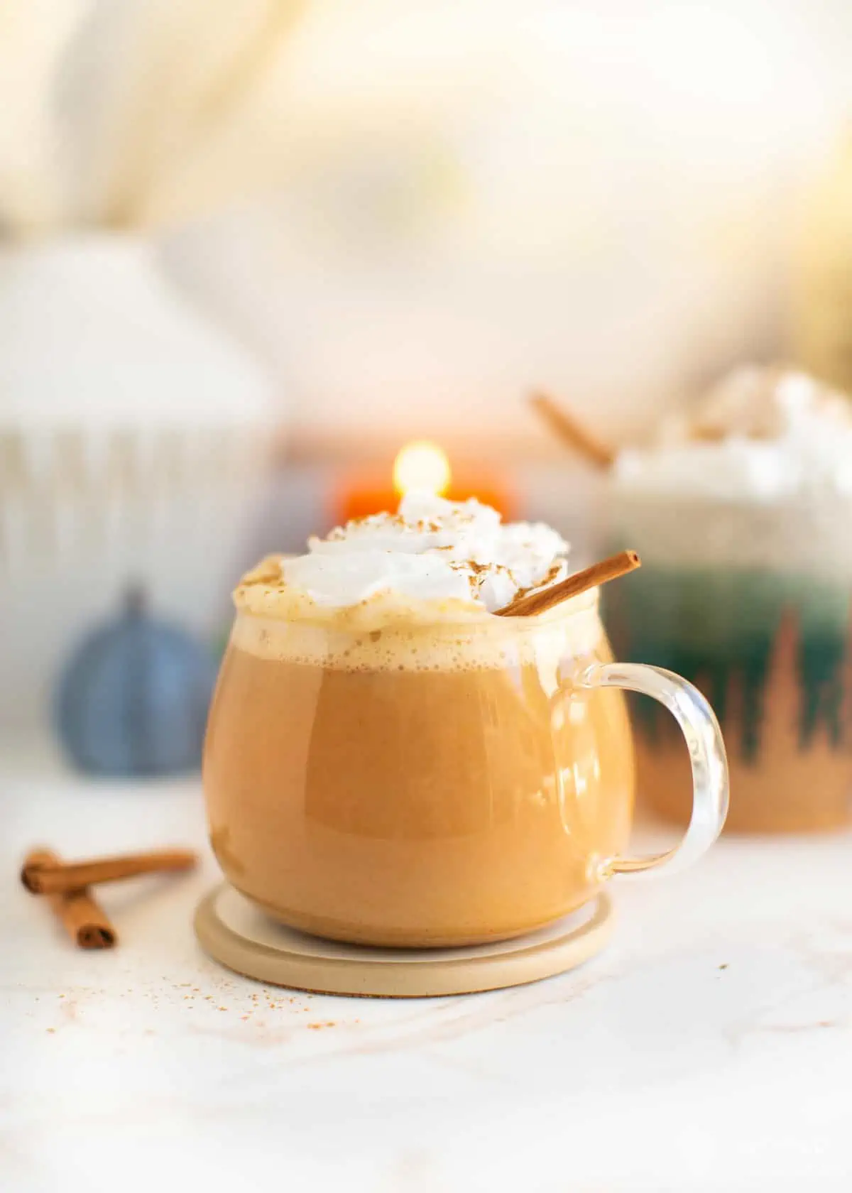 Side view of a glass mug filled with pumpkin spice latte, whipped cream, and a sprinkle of cinnamon.