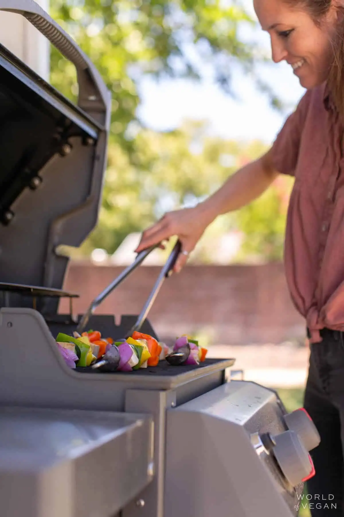 A hand holding tongs, flipping tofu kebabs over on the grill.