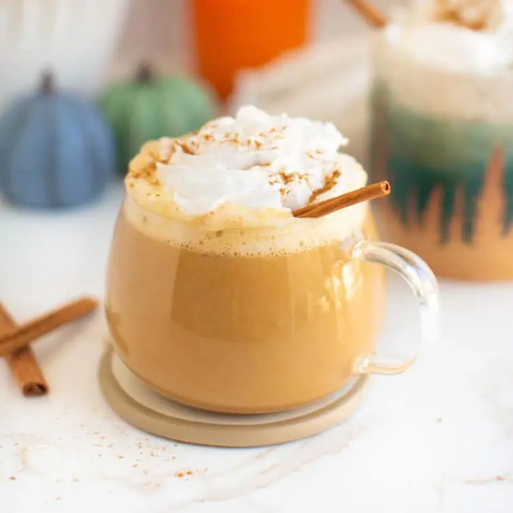 A clear glass mug filled with pumpkin spice latte and topped with vegan whipped cream.